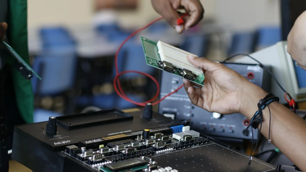 A hardware testing workbench with multiple PC rigs and an OLED monitor showing frame-rate telemetry.
